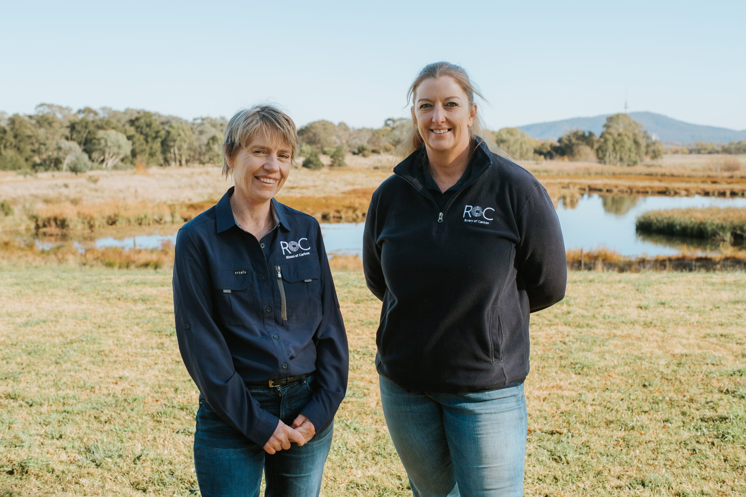 Rivers of Carbon Project Manager Lori Gould and Project Officer Alex James stand side-by-side smiling at Jerrabomberra Wetlands.